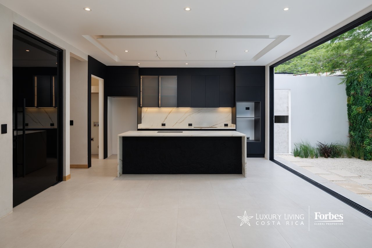 Modern kitchen with dark cabinetry and a large island opening onto a landscaped courtyard.