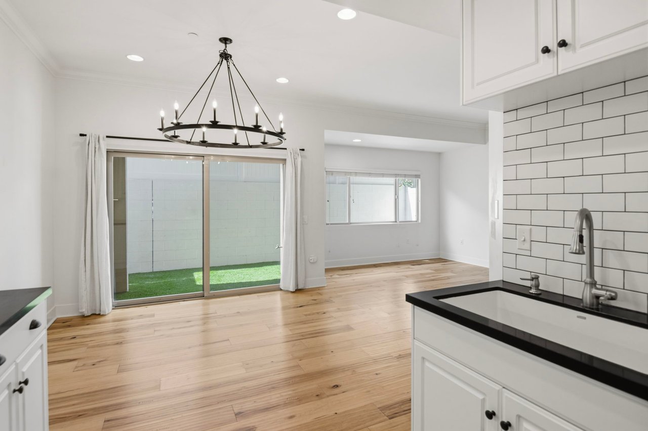 Dining area with iron chandelier, sliding glass door to private patio, hardwood floors, and open kitchen view