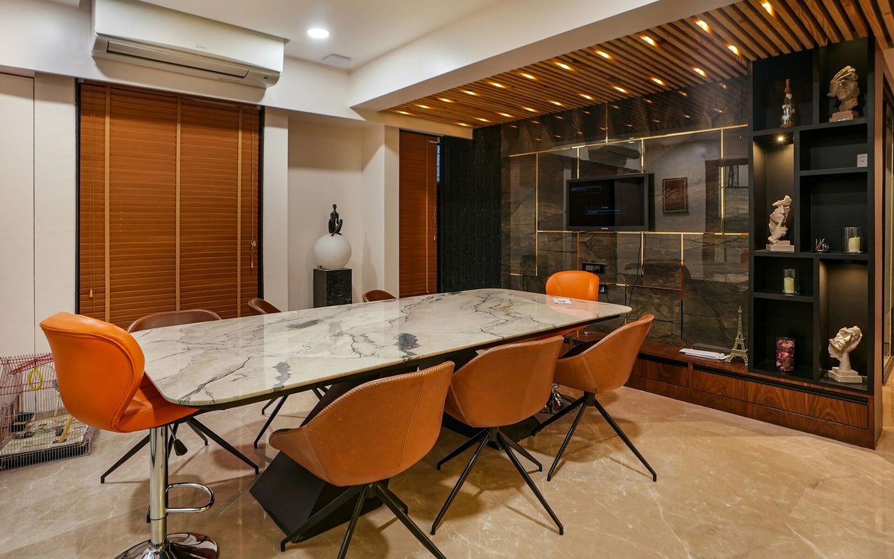 Modern dining area with a marble table, orange leather chairs, and dark built-in shelving.