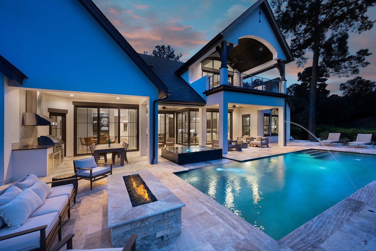 Modern home and swimming pool at dusk, with a stone patio, outdoor kitchen, and fire feature.