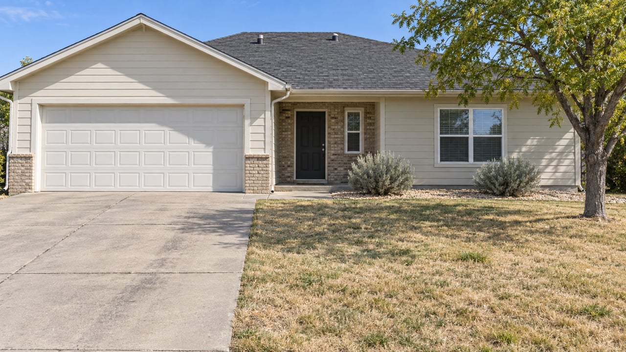 One-story cream-sided house with a double garage, tan brick entry, driveway, and dry lawn.