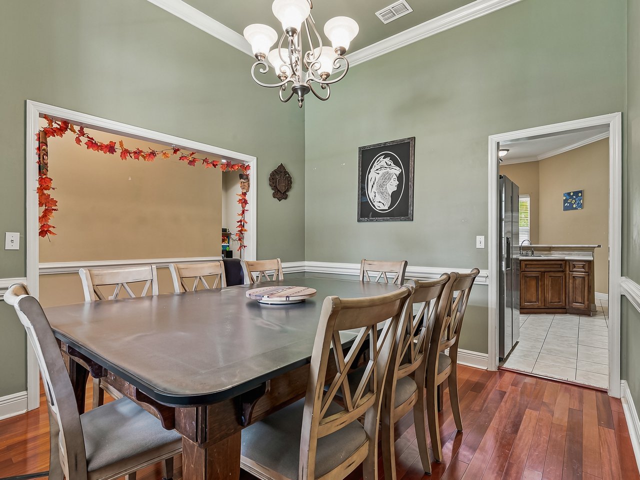 Dining room with a large wood table, matching chairs, sage green walls, and a chandelier.