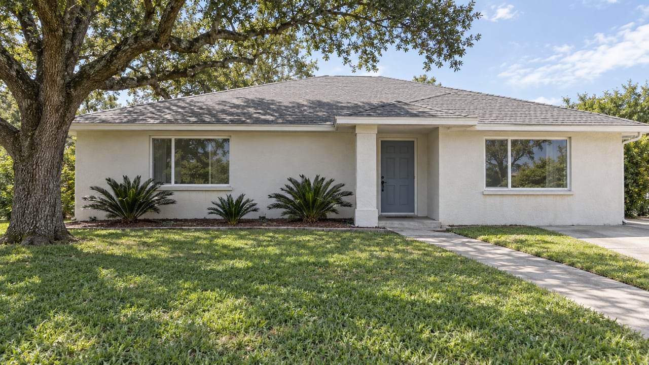An off-white single-story home behind a broad lawn, with a spreading live oak and a simple covered entrance.
