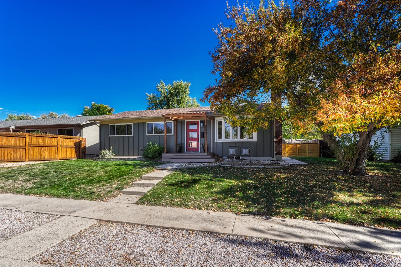 Front exterior in daylight with board-and-batten siding, a red front door and a large tree in fall color
