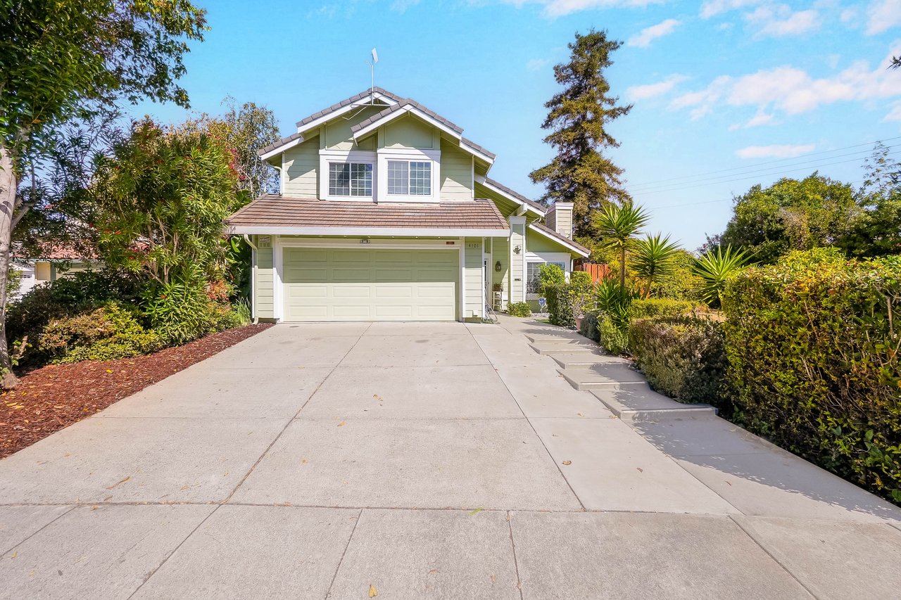 Two-story green house with a wide double garage, broad driveway, and landscaped entry.