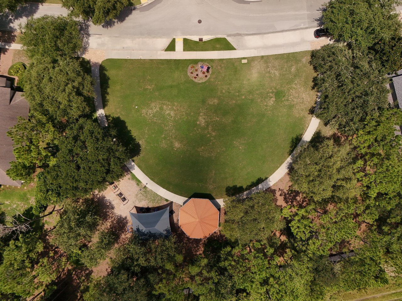 Aerial view of a neighborhood park with a broad lawn, mature trees, and shade structures.