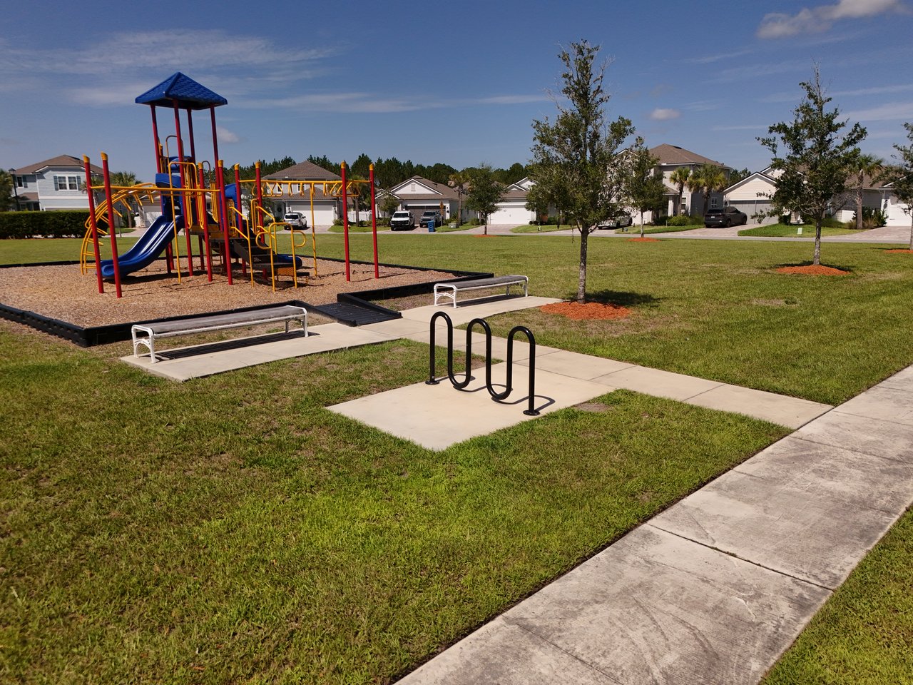 Neighborhood playground with colorful climbing equipment, a paved path, and a bicycle rack.