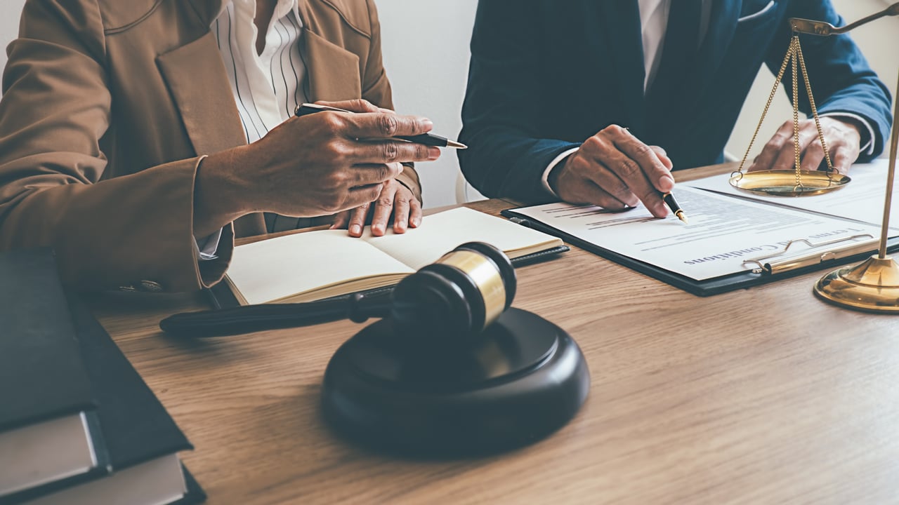 Two people review legal documents beside a judge’s gavel and scales of justice.