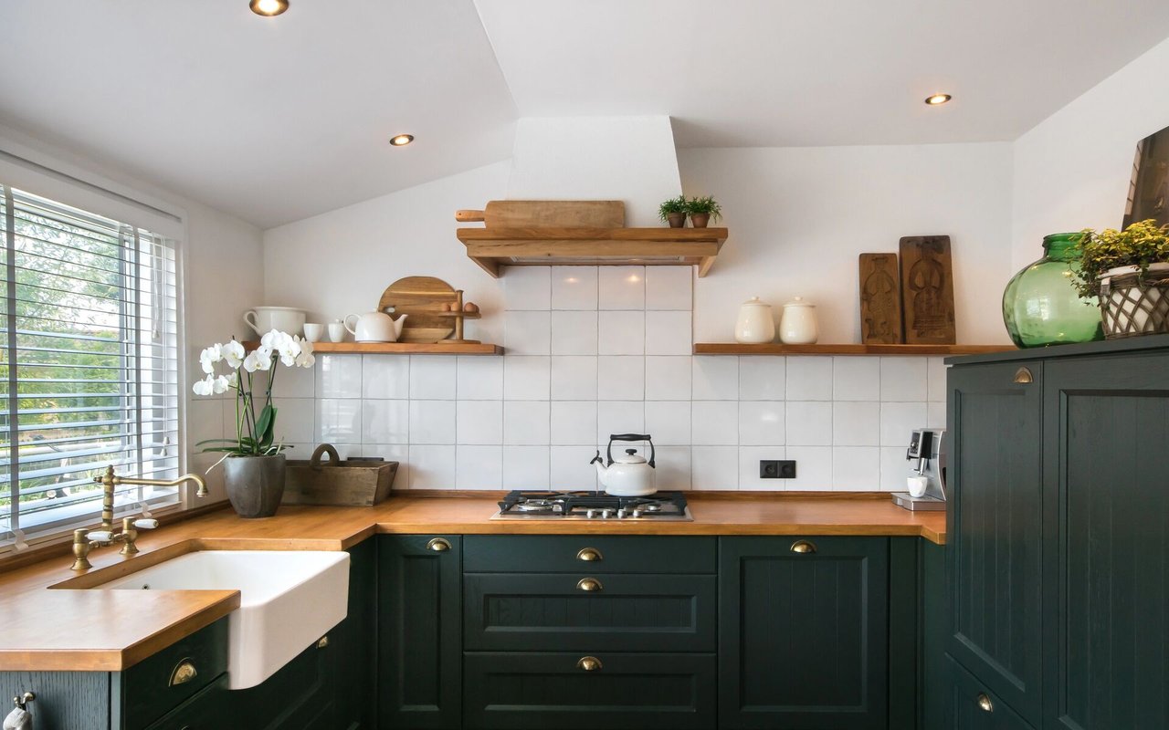 Kitchen with dark green cabinets, warm wood counters, and a white farmhouse sink beneath a bright window.