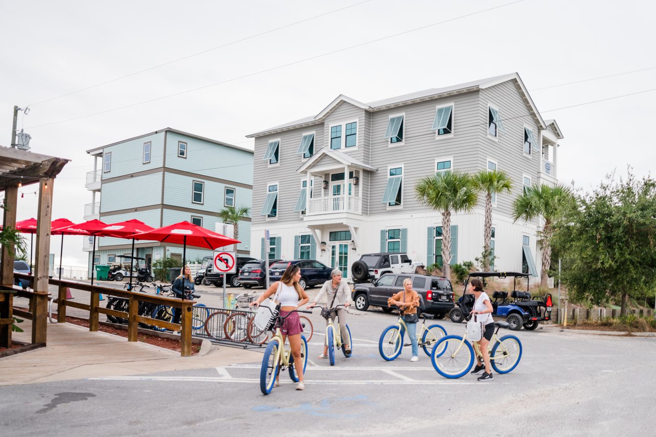 Visitors with beach-cruiser bikes gathered below pastel two-story cottages and red cafe umbrellas in Grayton Beach on 30A, Florida