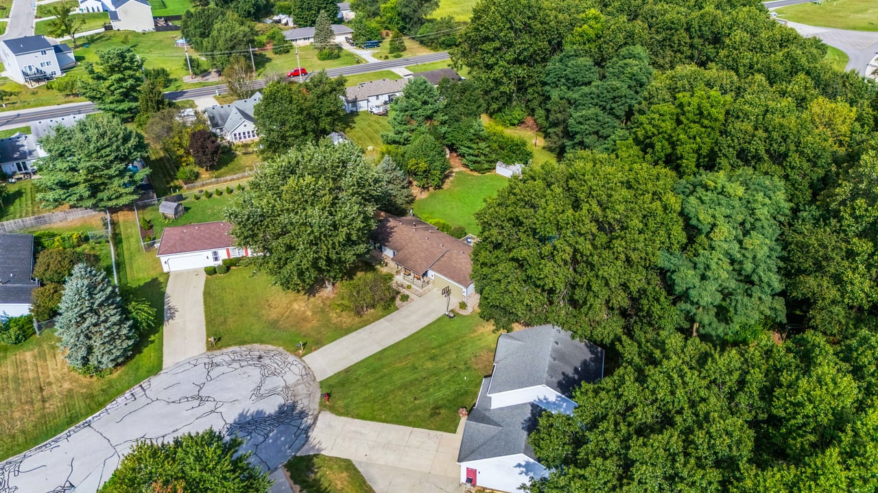 Aerial view of a home beside dense trees, with a long driveway and nearby cul-de-sac.