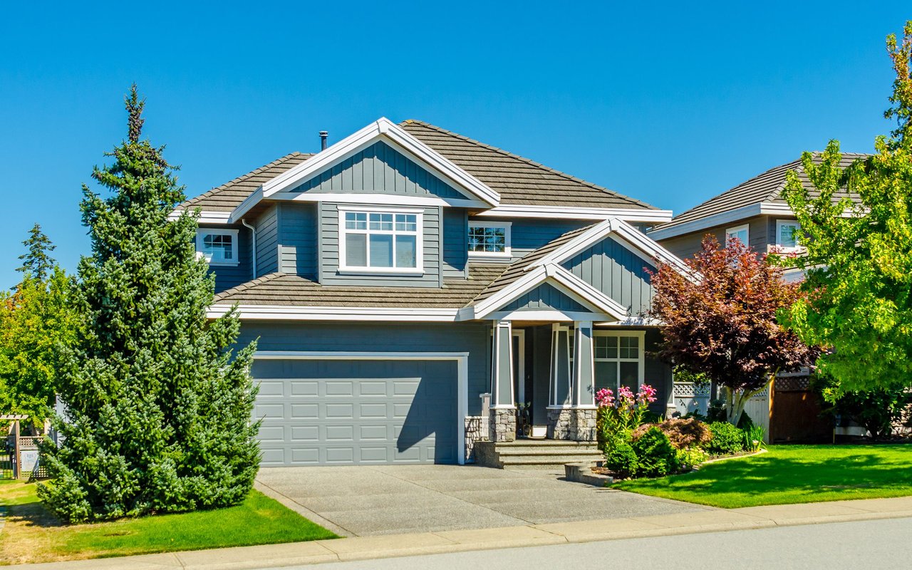 Two-story blue-gray house with a double garage, covered entry, and landscaped front yard.
