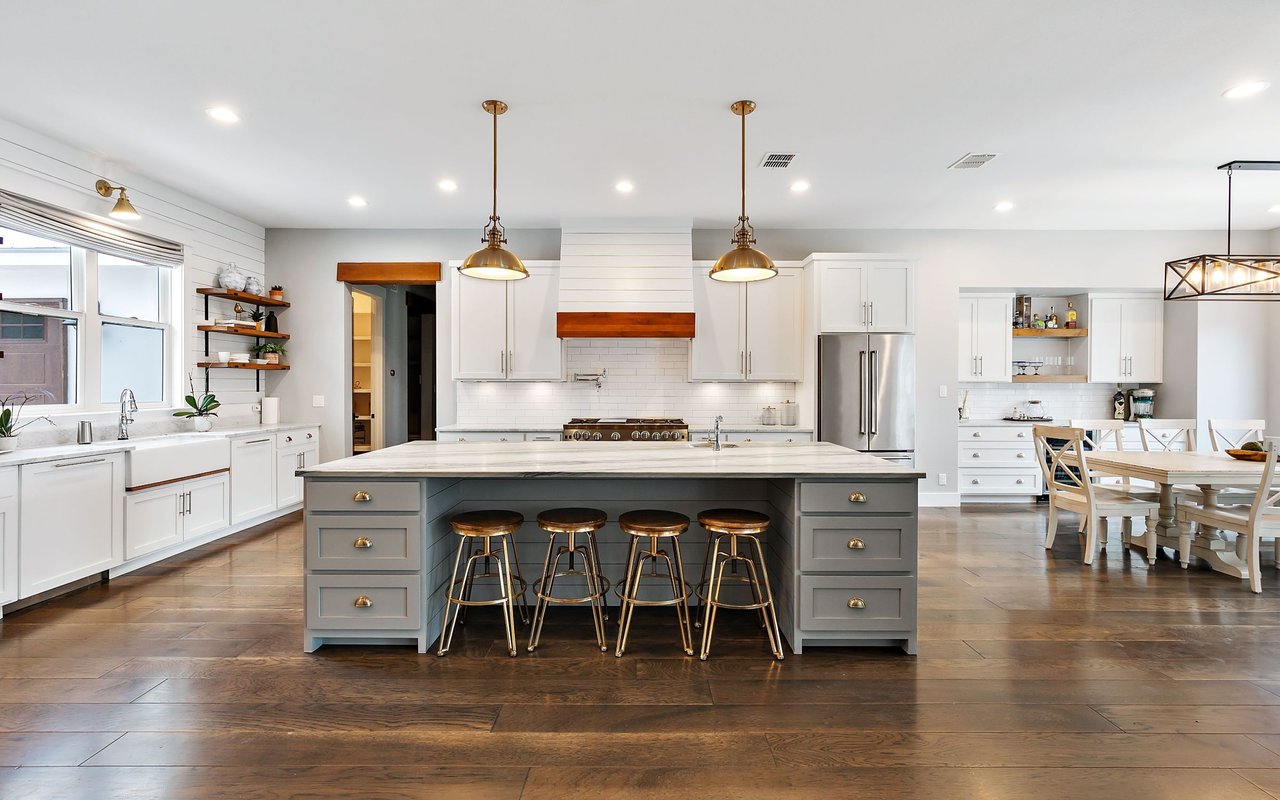 Bright kitchen with a large gray island, four bar stools, white cabinets, and an adjoining dining area.