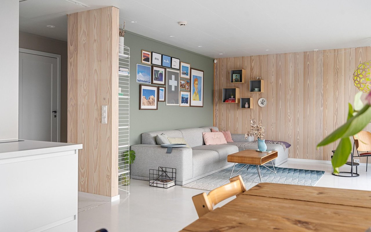 Open-plan living and dining room with a gray sectional, pale wood paneling, and a wooden table.