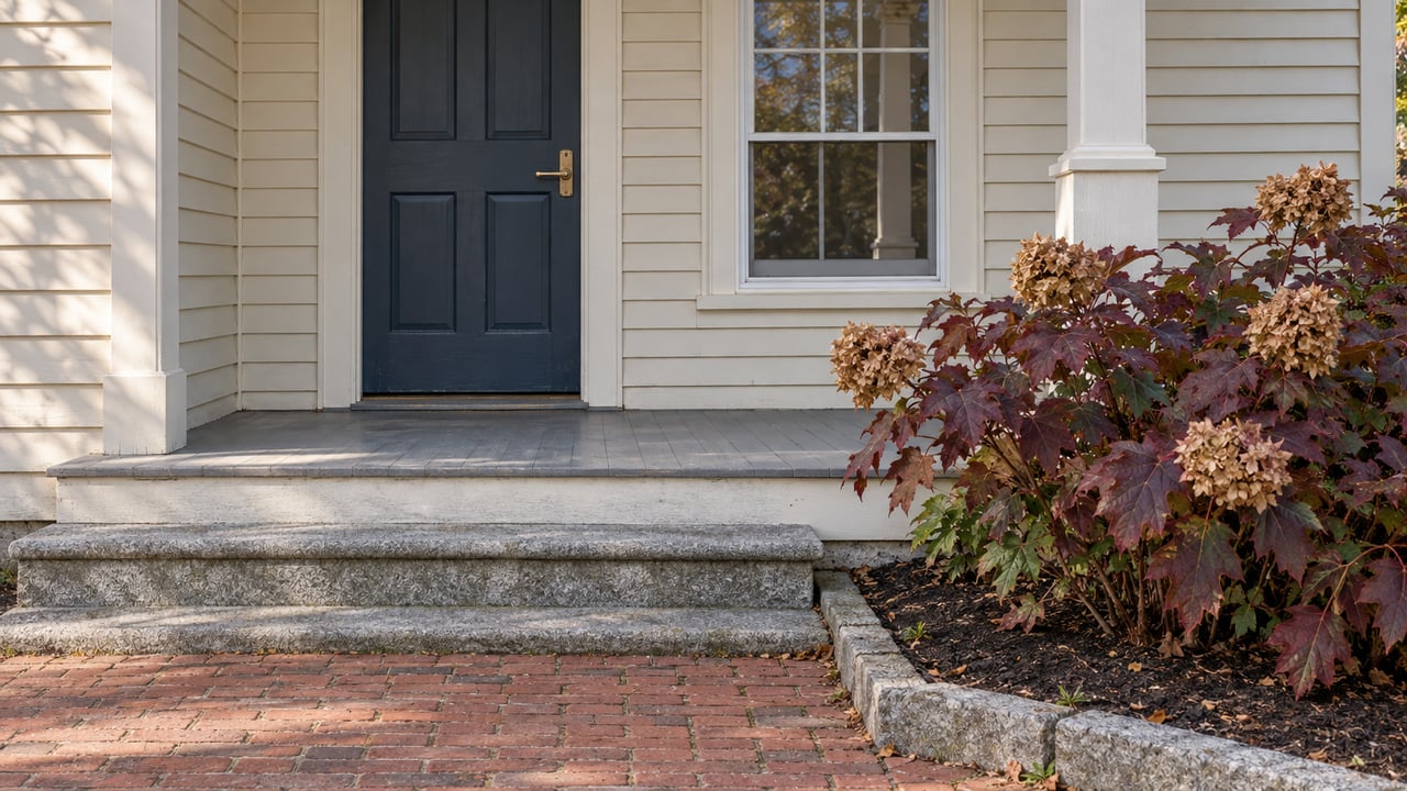 Ivory clapboard home entrance with a blue door, granite steps, brick approach and burgundy oakleaf hydrangea.