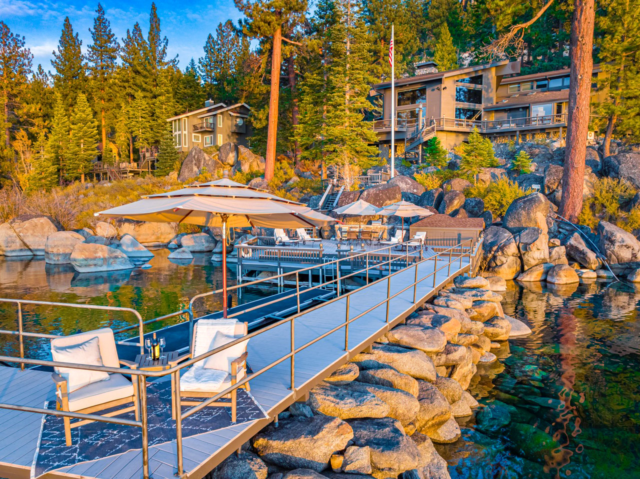 Lakefront home above a rocky shore, with a furnished dock extending over the water.