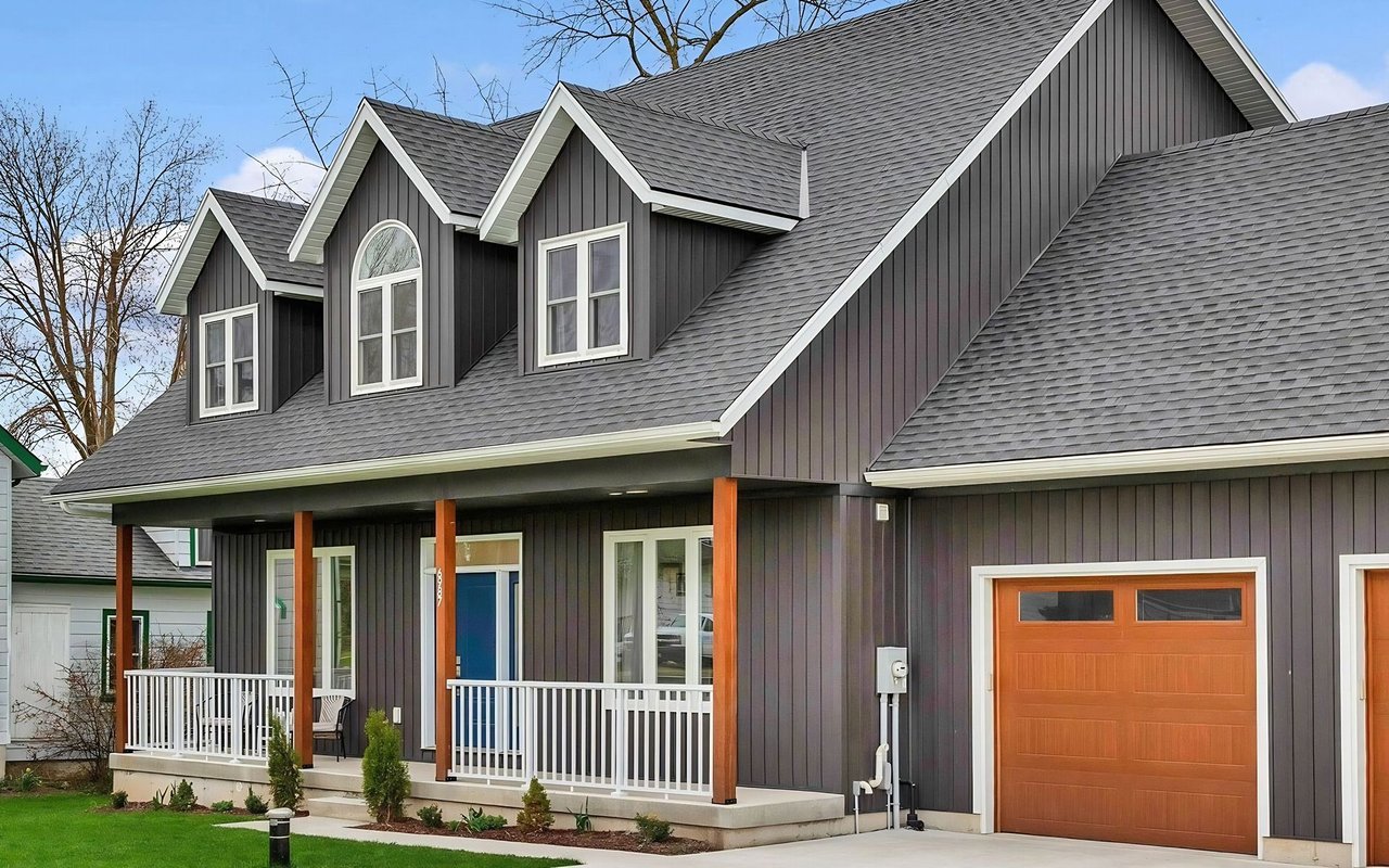 Two-story dark-sided home with white-trimmed dormers, a covered porch, blue front door, and attached garage.