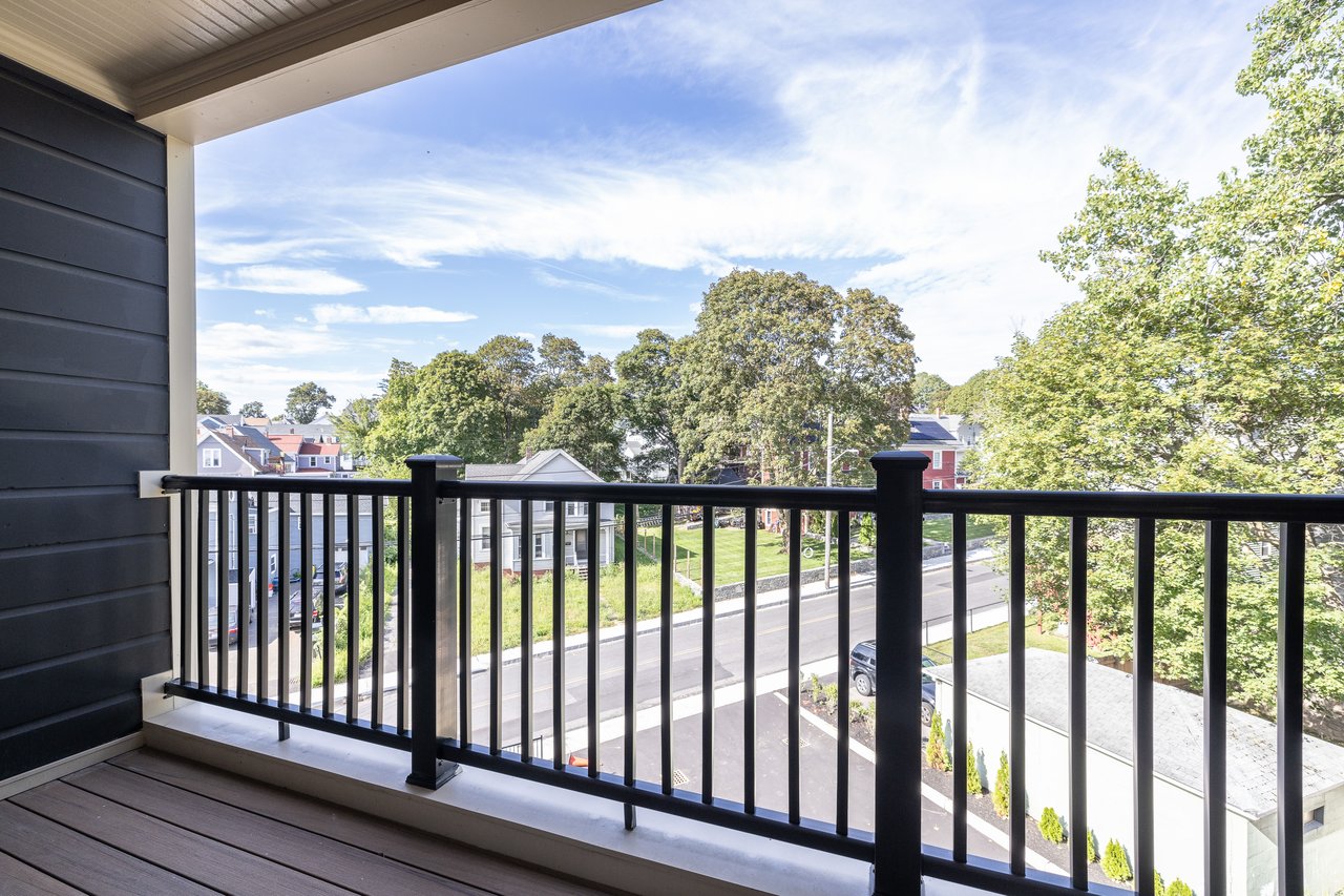 Covered balcony overlooking a residential street and leafy neighborhood trees.