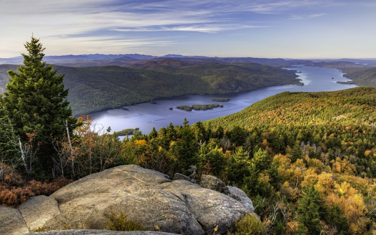 Lake George and its islands among forested mountains, viewed from a rocky overlook in autumn.