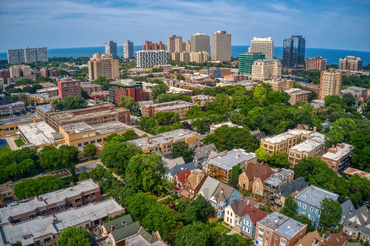 Aerial view of a leafy neighborhood and high-rises beside a blue lake.