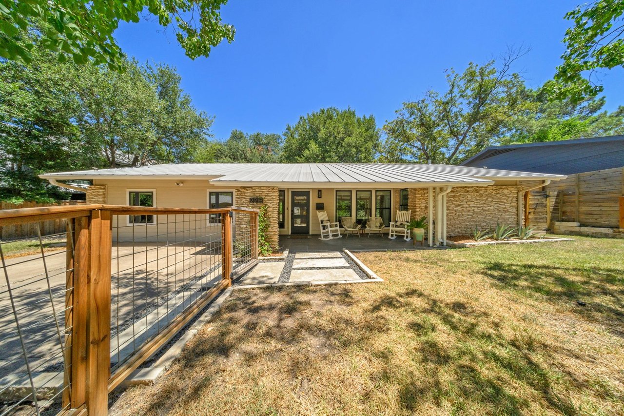 Single-story home with a light metal roof, stone accents, and a fenced front walkway.