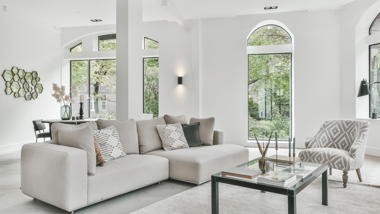 Bright living room with a light sectional, patterned armchair, and tall arched windows.