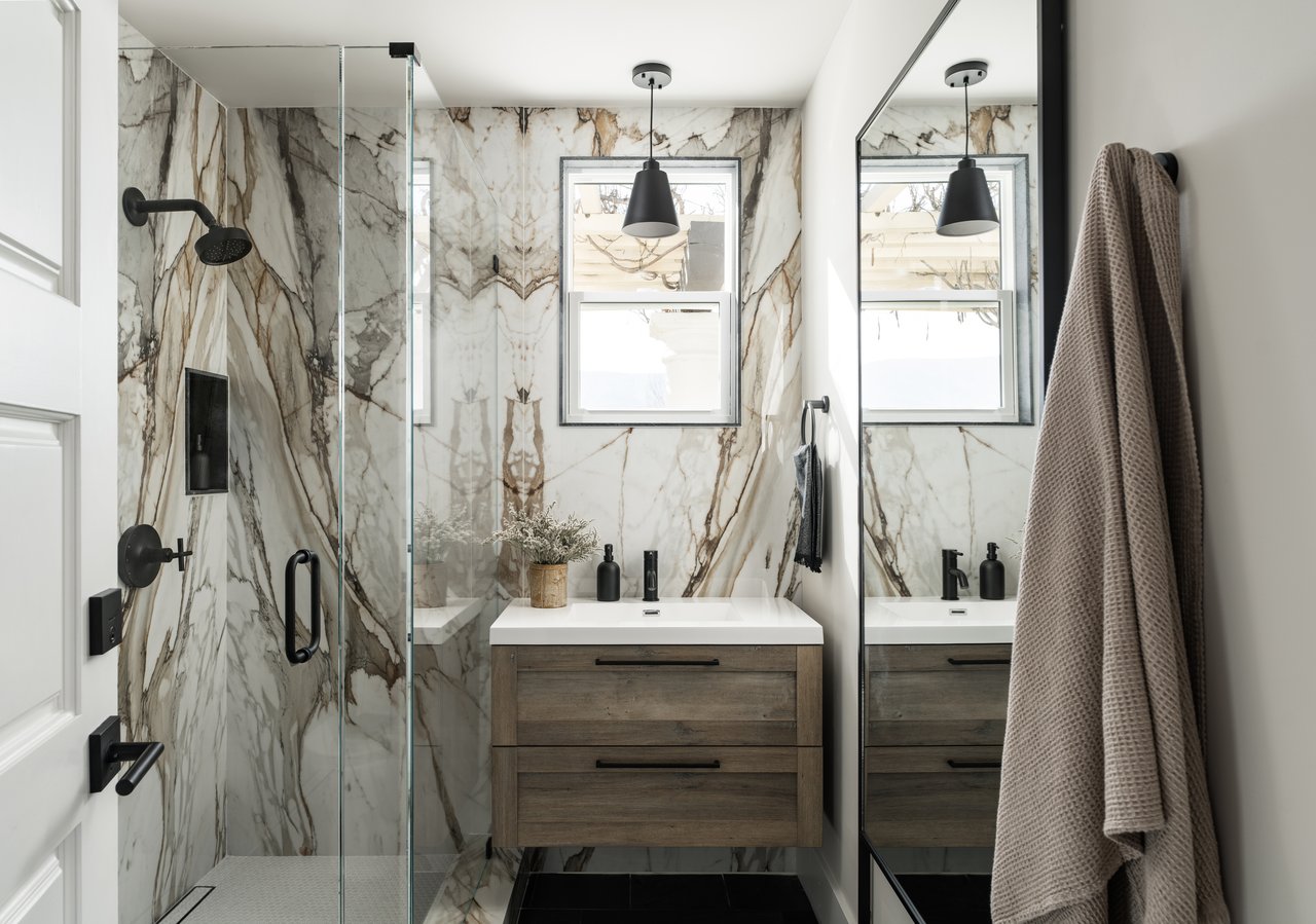 Modern bathroom with veined marble walls, a glass shower, and a floating wood vanity.