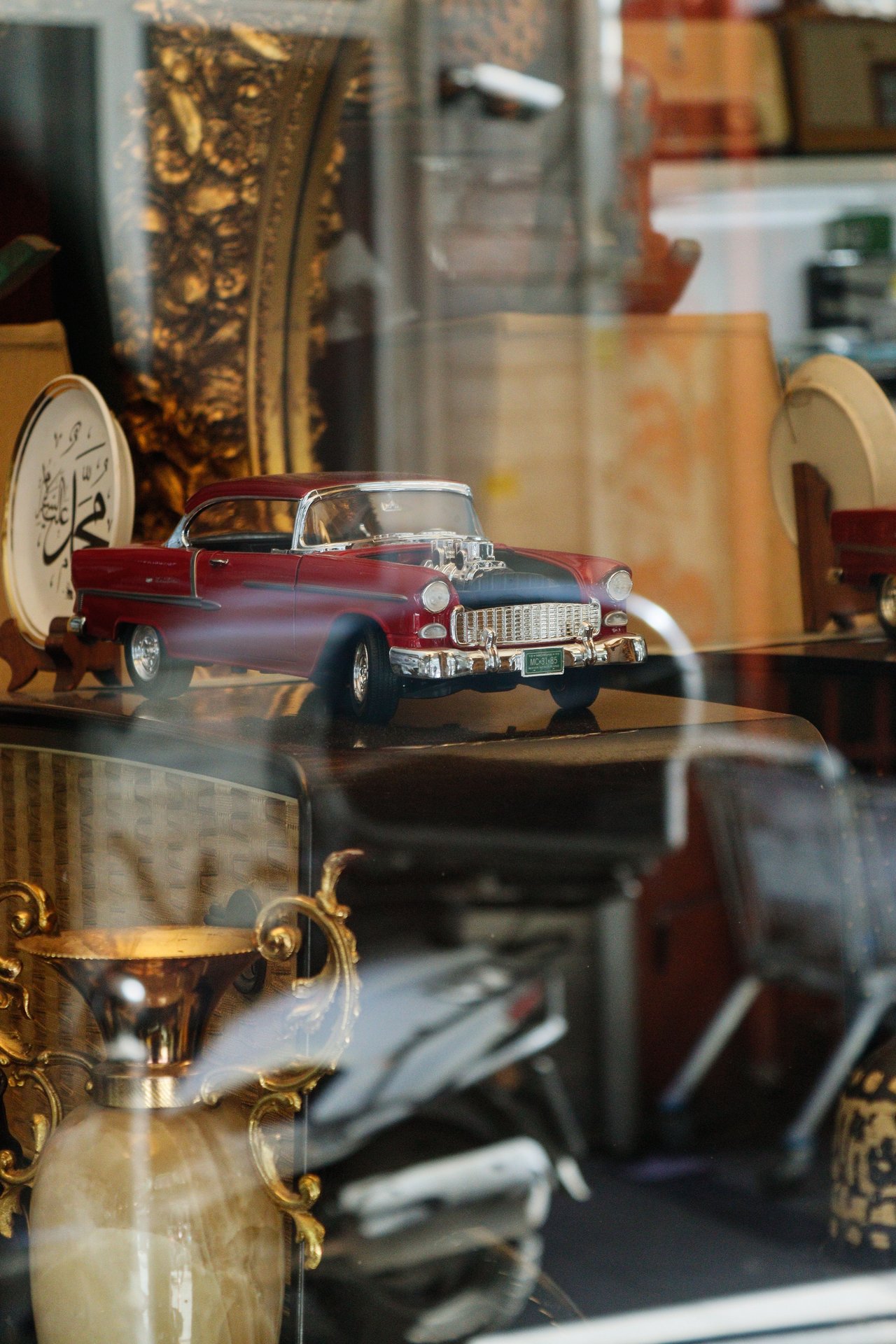 Red miniature vintage Chevrolet displayed among antiques behind glass.