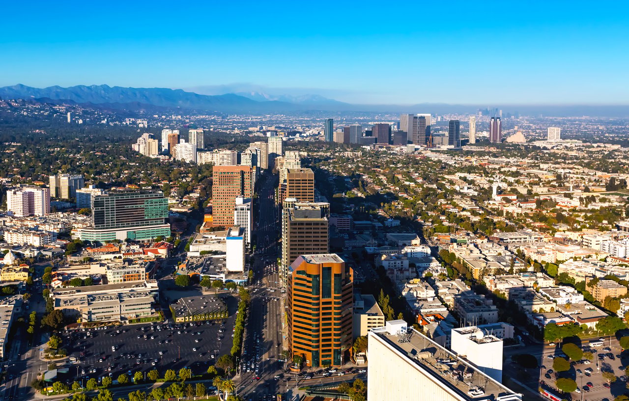 Aerial view of Century City’s high-rises and surrounding Los Angeles neighborhoods beneath distant mountains.