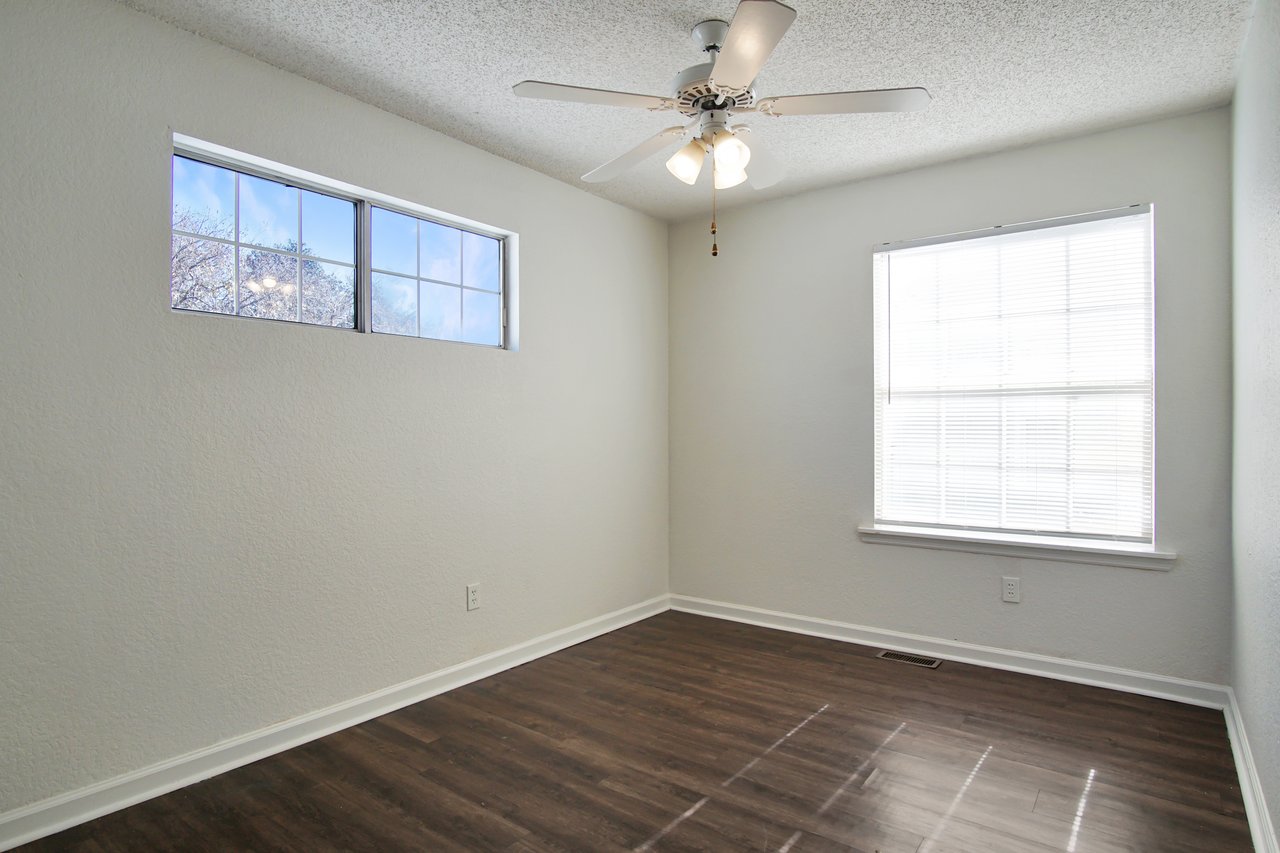 Empty room featuring hardwood floors and a ceiling fan, creating a spacious and airy atmosphere.