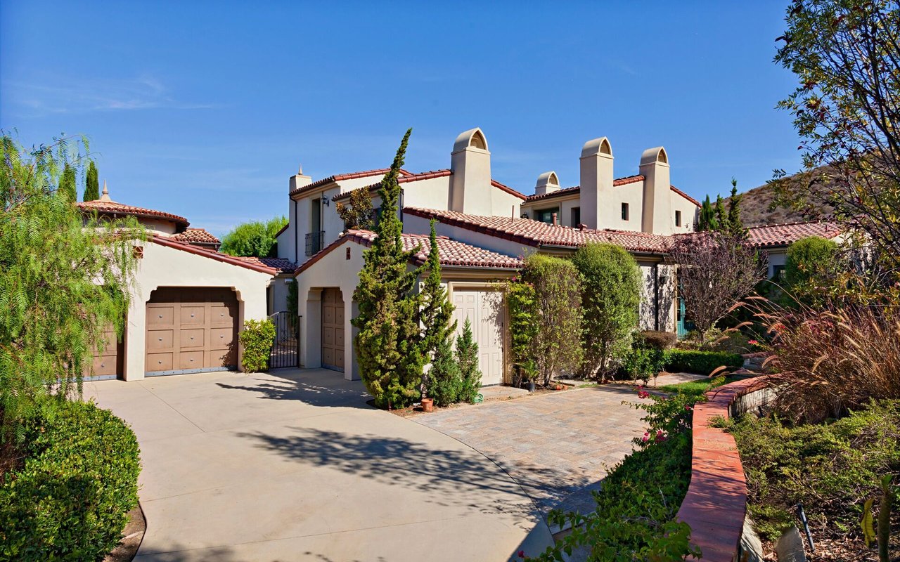 Stucco home with red tile roofs, multiple chimneys, an attached garage, and landscaped grounds.