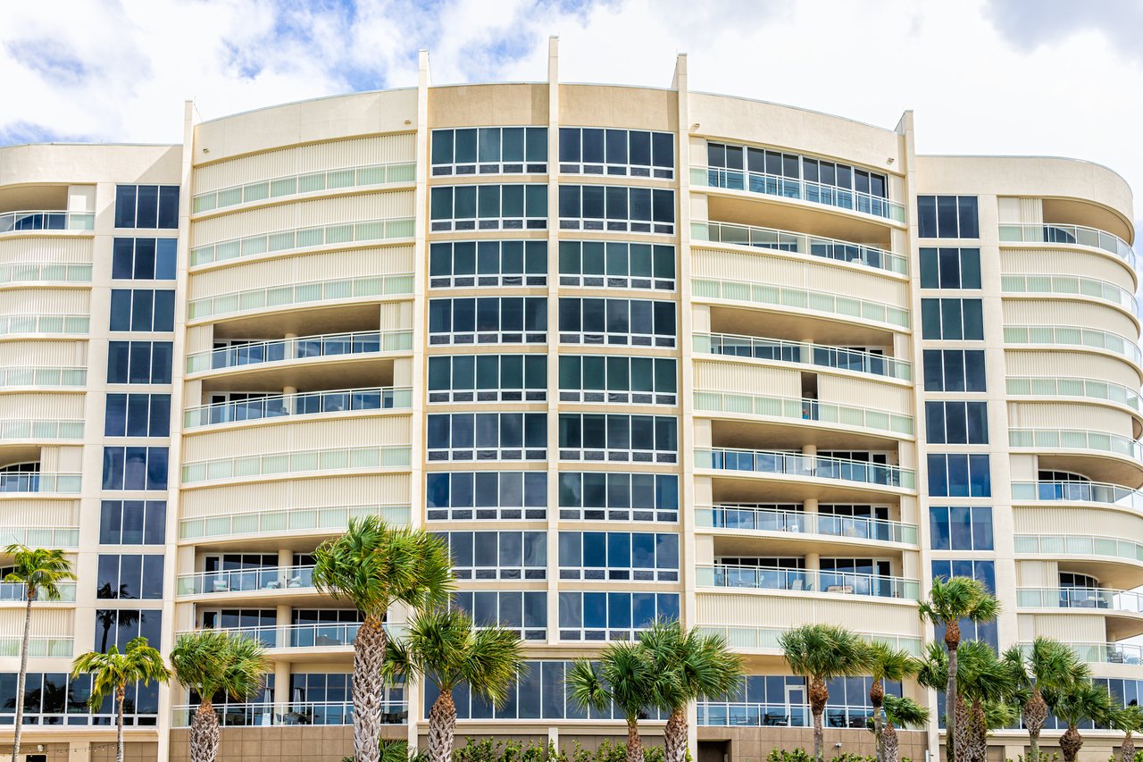 Modern condominium building with curved balconies and palm trees along the front.