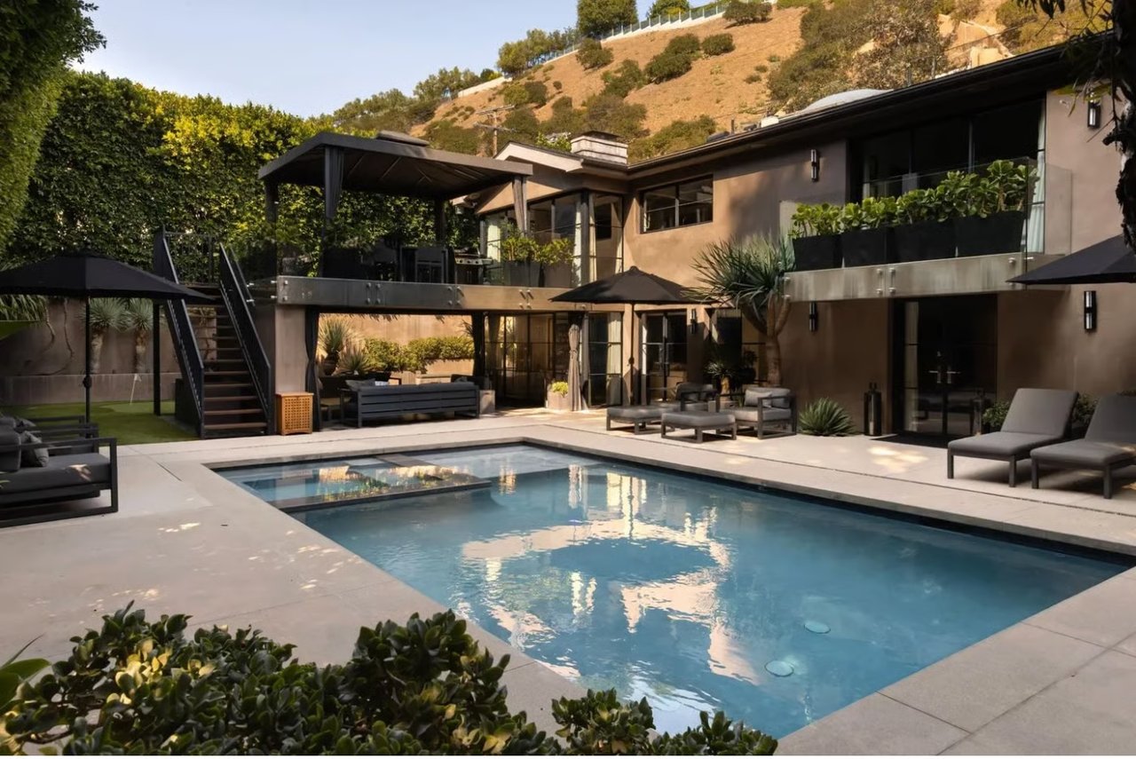 Modern home with a large pool, tiered patio, and hillside backdrop.