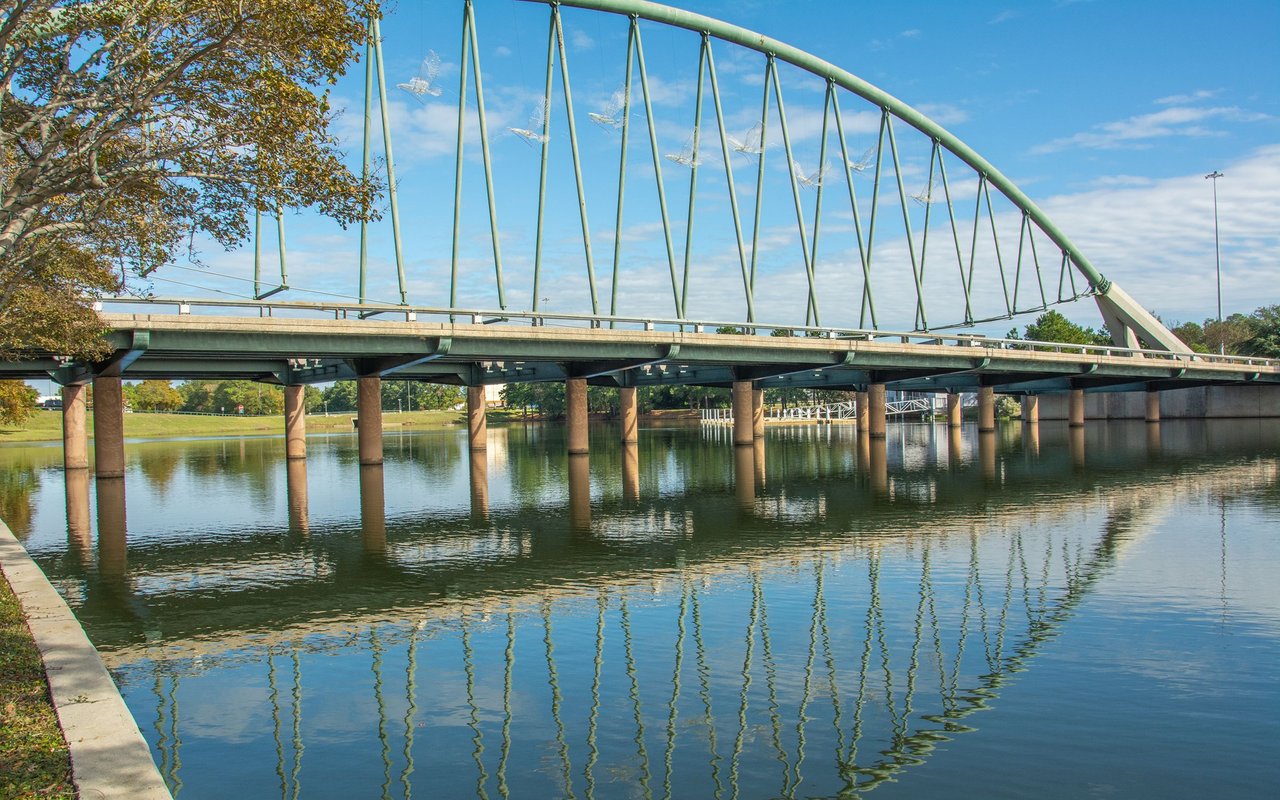 Green arched bridge spanning calm water, reflected beneath a blue sky.