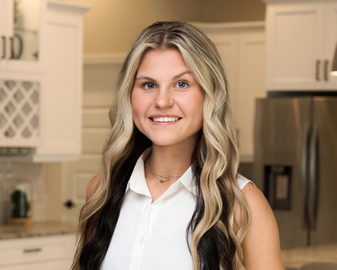 Caydence Warthen smiling in a white blouse in a kitchen.