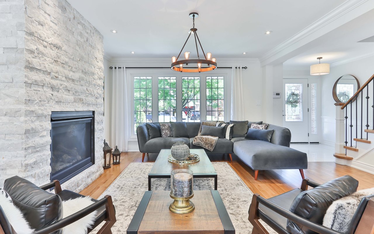 Living room with a stone fireplace, gray sectional, leather armchairs, and tall windows.