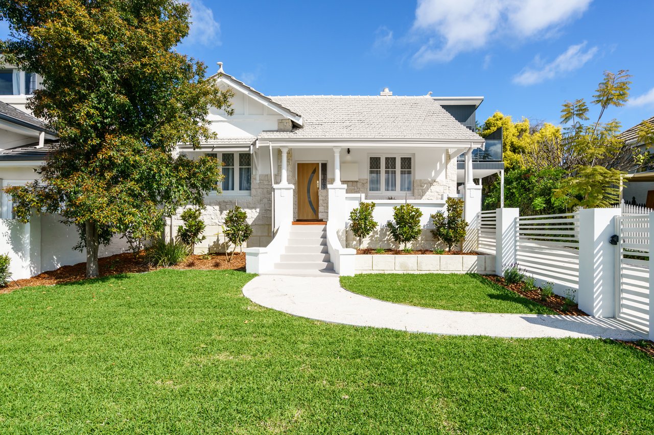 White stone-front house with a covered porch, curved walkway, and broad lawn.