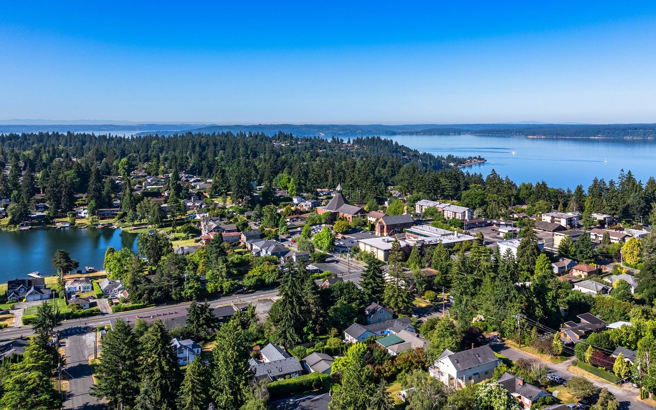 Aerial view of Burien homes among trees, with a small lake and broad bay beyond.