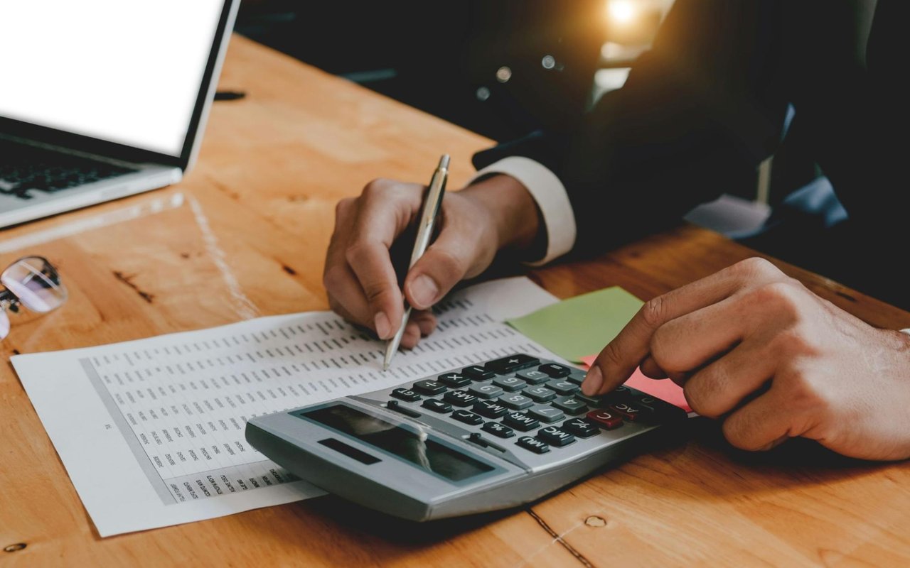  A close-up shot of a person's hands working on financial calculations at a wooden desk. 