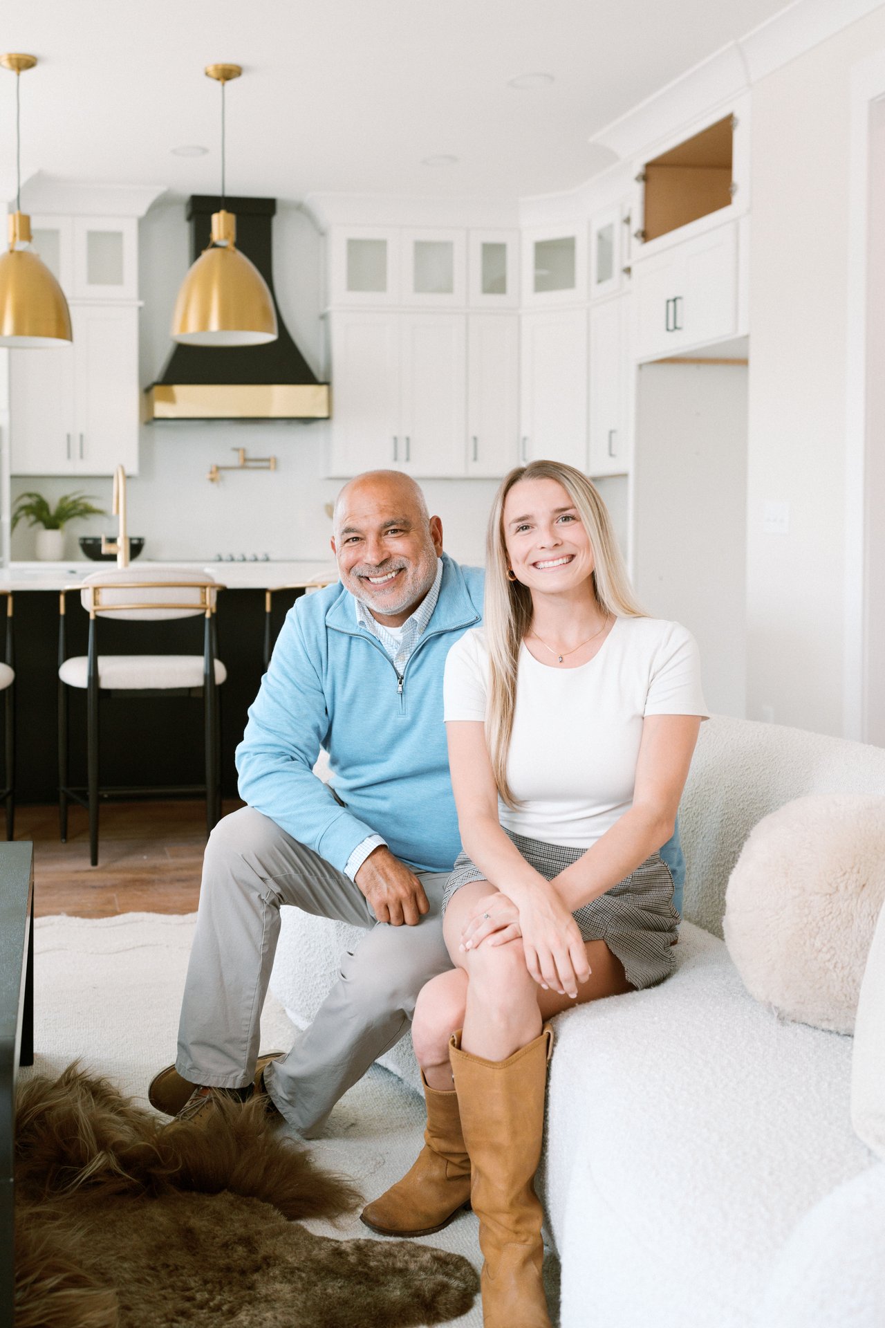 Two smiling adults seated together in a bright modern kitchen, with a dog in the foreground.
