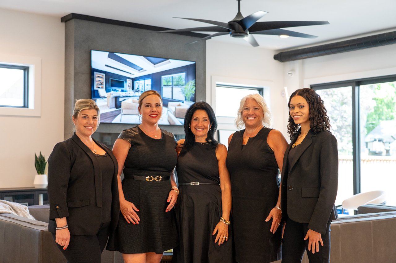 Five real estate team members pose together in a bright, modern office lounge.
