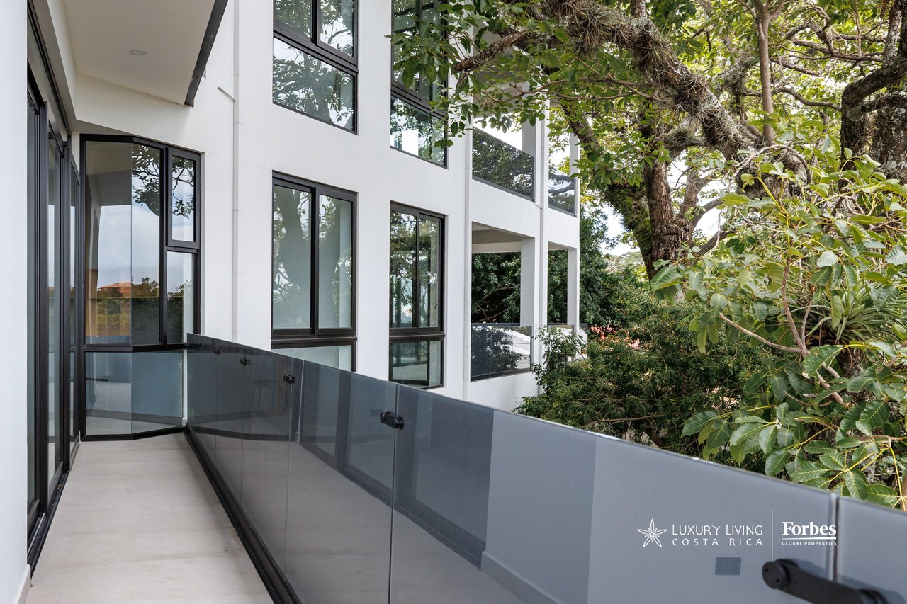 Modern apartment balcony with a gray glass railing overlooking leafy trees.