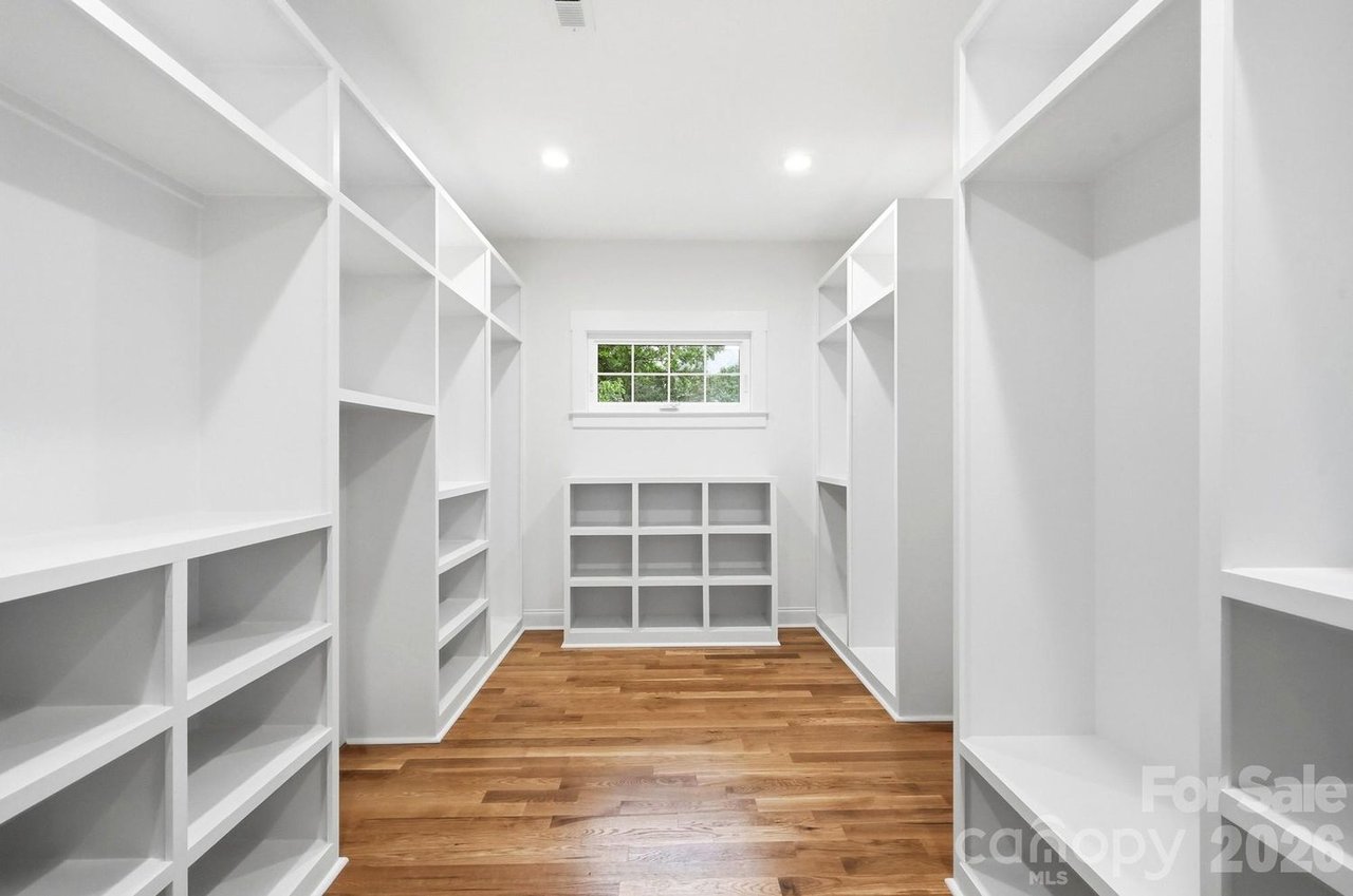 Walk-in closet with white built-in shelving, hardwood floors, and a small rear window.