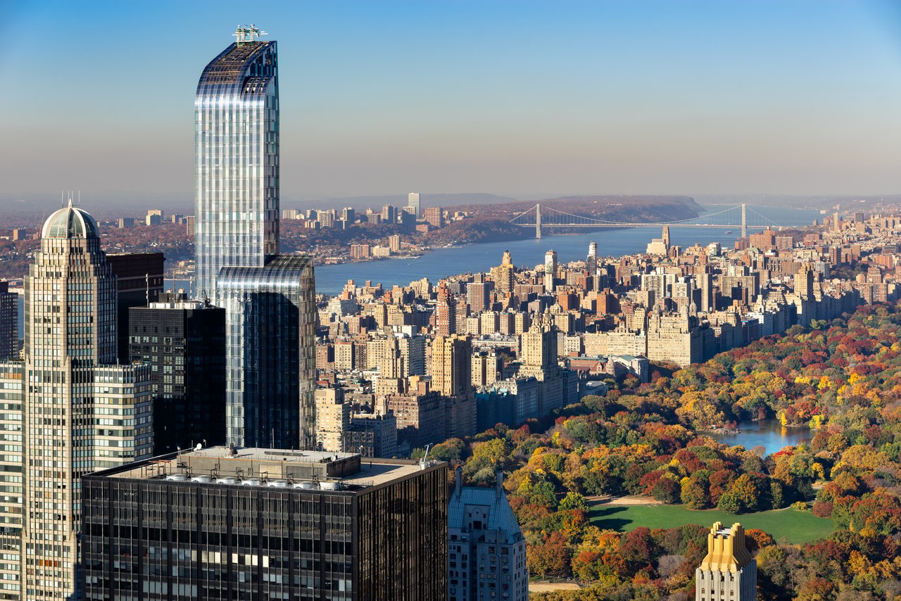 Manhattan skyline and Central Park in autumn, with a suspension bridge in the distance.