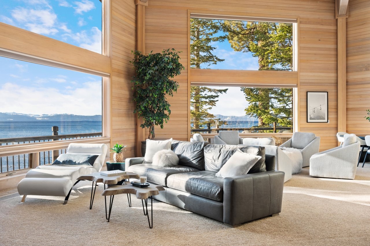Living room with wood-paneled walls, lake and mountain views through large windows, and a gray sofa.