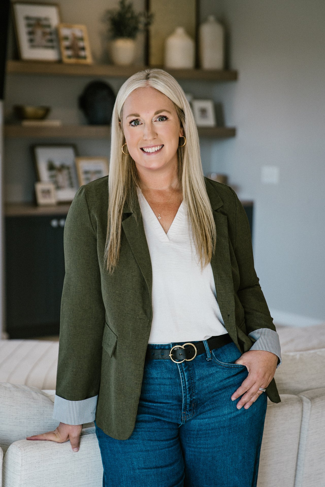 Hollie Engle smiling in a green blazer and jeans, leaning against a sofa.