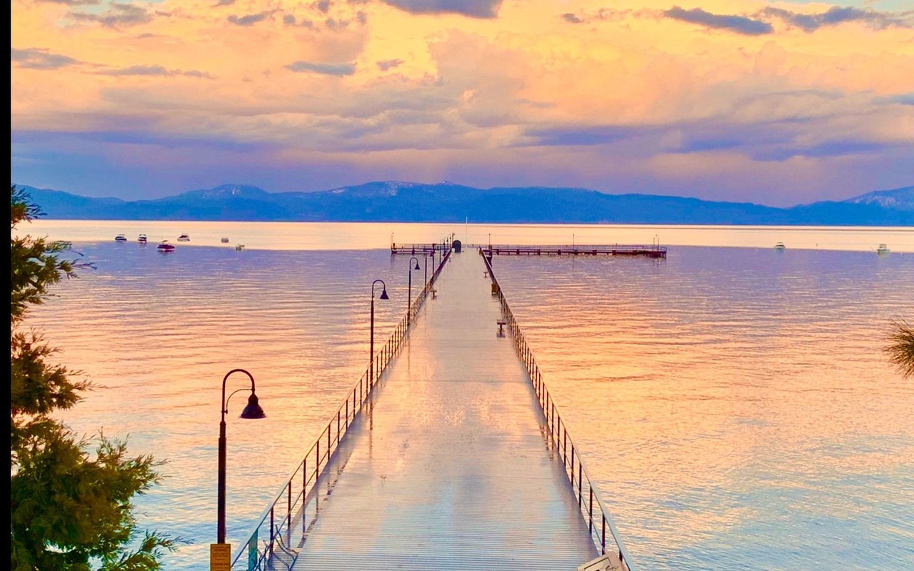 Pier extending into Lake Tahoe at sunset, with boats and mountain ridges across the water.