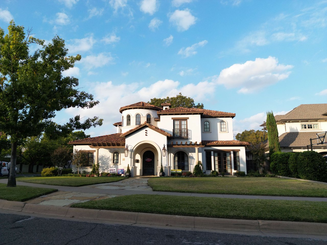 White stucco home with terracotta tile roof, arched entry, and landscaped front lawn.