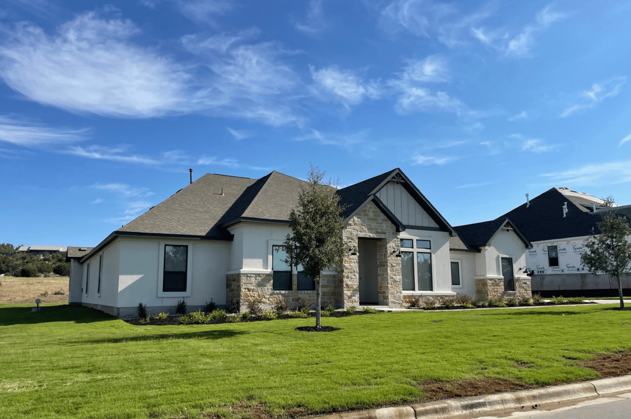 Single-story stucco house with stone entry accents and a broad green lawn.