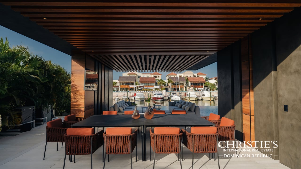 Covered villa terrace with a long dining table overlooking boats in the marina.